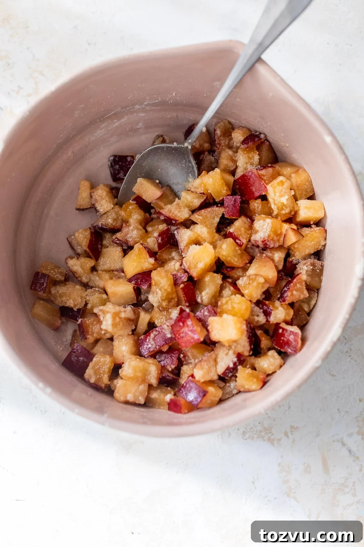 using a spoon to stir the plum filling for plum bars in a pink bowl.