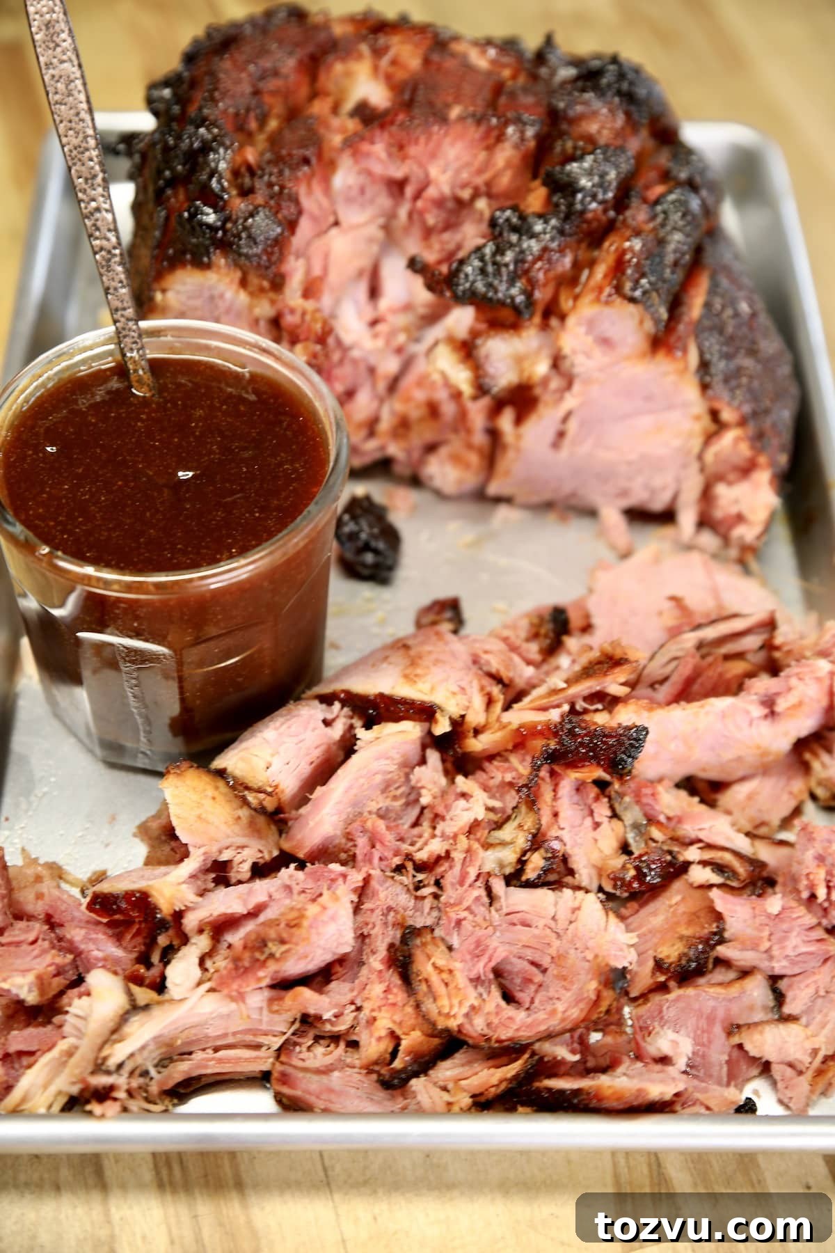 Blackberry glazed ham, partially sliced into chunks with sauce on a sheet pan.