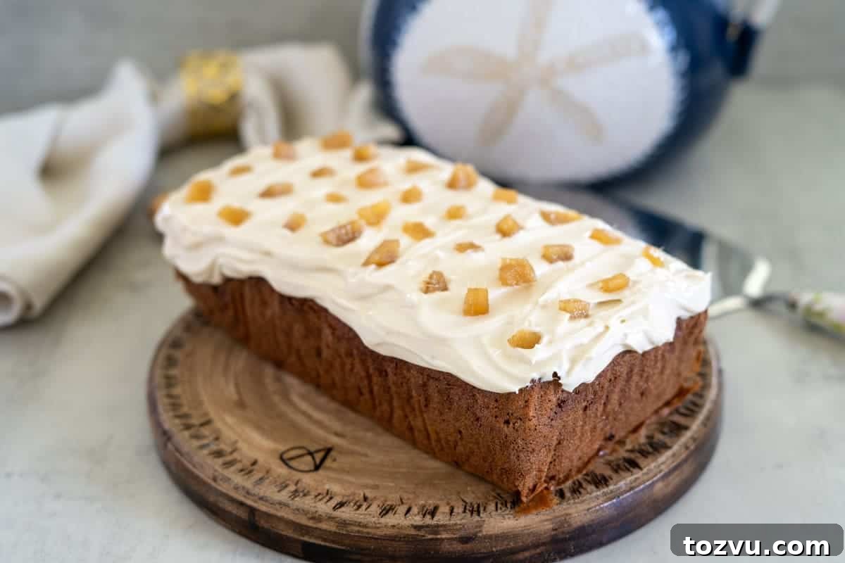 Ginger cake loaf with cream cheese frosting, adorned with candied ginger pieces, elegantly placed on a wooden board.