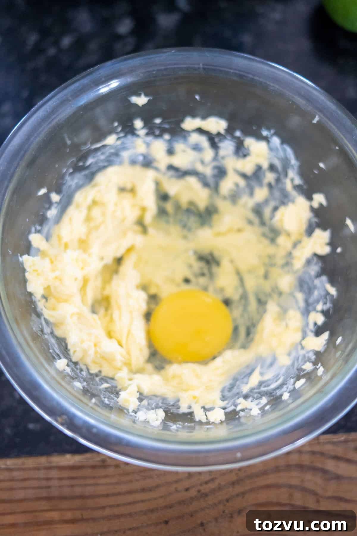 A glass bowl with softened butter and a raw egg awaits on the dark countertop, ready to be transformed into a delicious ginger cake.