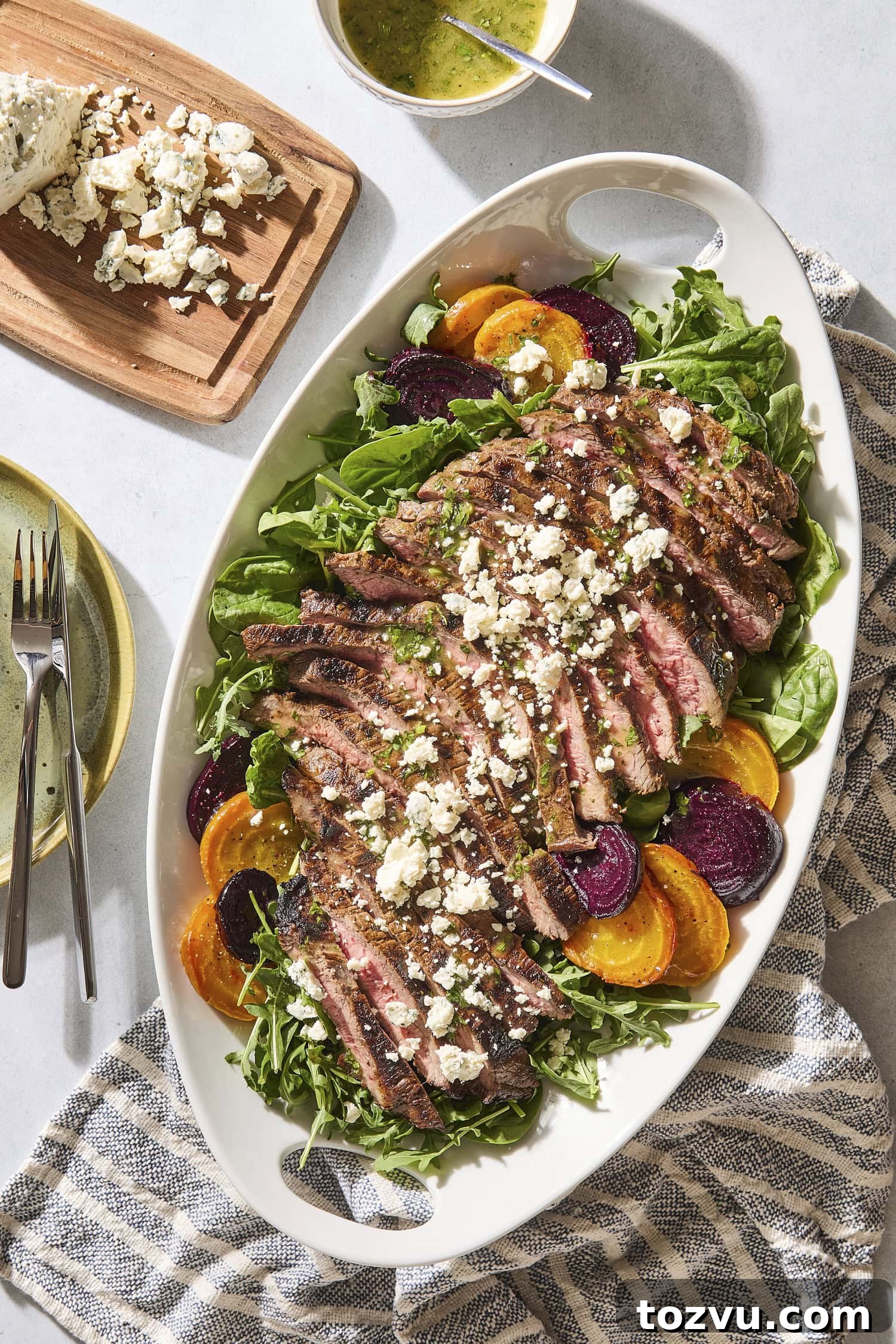 Grilled Steak with Roasted Beet and Goat Cheese Salad 3 Grilled steak and beet salad with crumbled blue cheese on top with plates to the side.