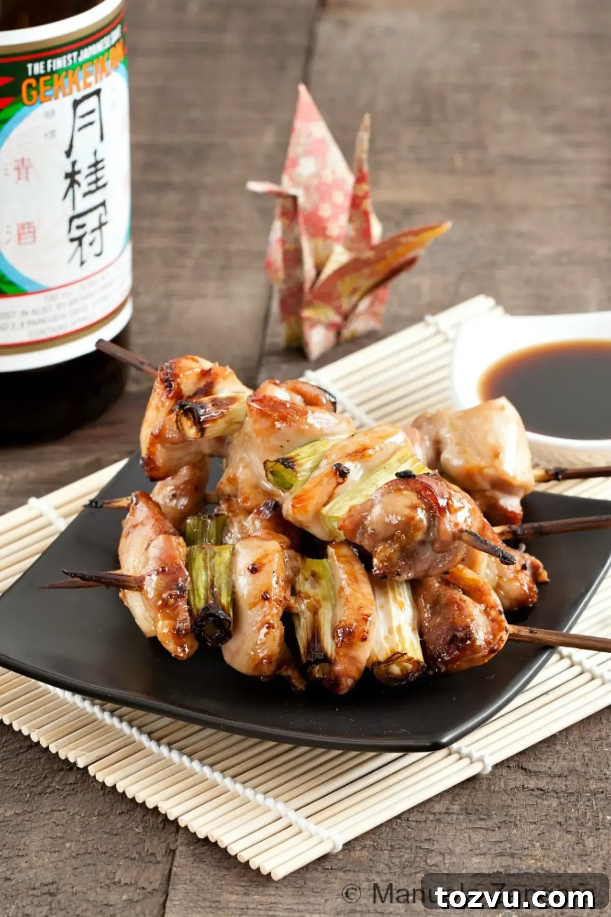 Yakitori: Authentic Japanese Grilled Chicken Skewers Recipe 6 Grilled chicken skewers with spring onions glazed in a soy-based sauce, served on a black plate.