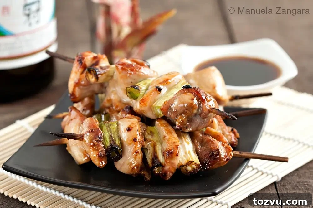 Yakitori: Authentic Japanese Grilled Chicken Skewers Recipe 7 Finished yakitori chicken skewers with spring onions served on a black plate with dipping sauce.