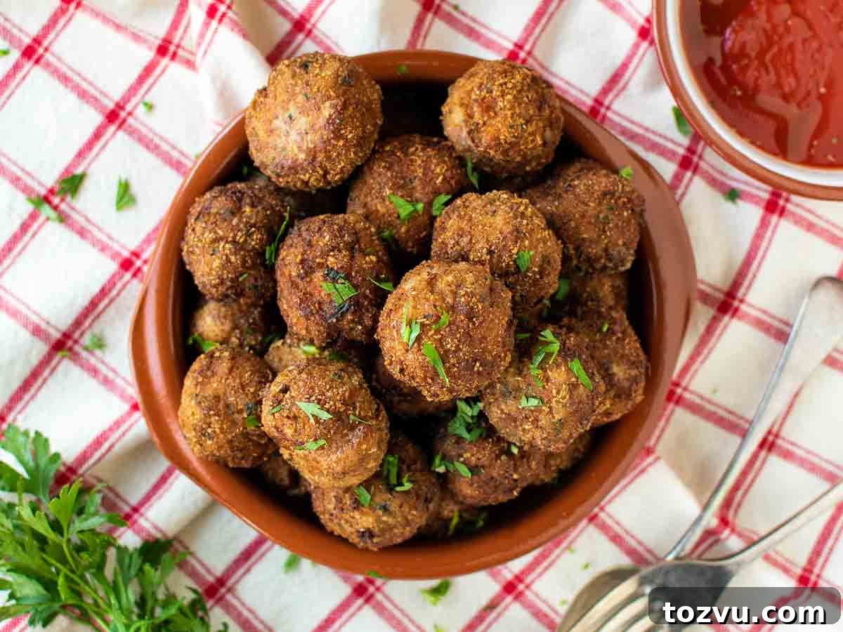 Crispy Fried Meatballs with Garlic Dipping Sauce 8 Brown meat balls piled onto a plate on a red and white checked tablecloth.