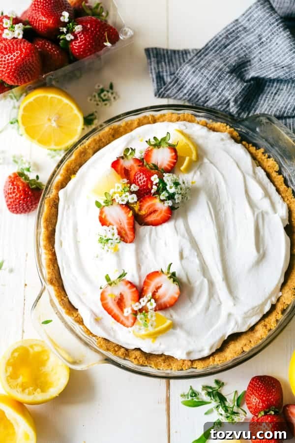 Lemon Pudding Pie in a clear pie pan with fresh strawberries and lemons on the side.