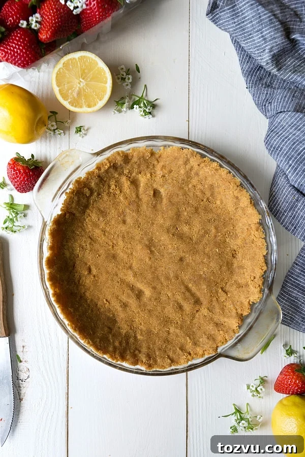 Pie crust with lemons and strawberries Pie crust in a clear pie pan with fresh lemons and strawberries on the side.