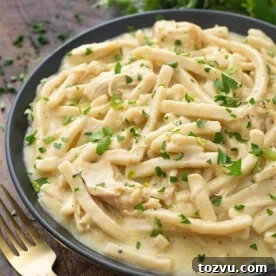 Instant Pot Chicken and Noodles in a black bowl on wooden board next to two golden forks
