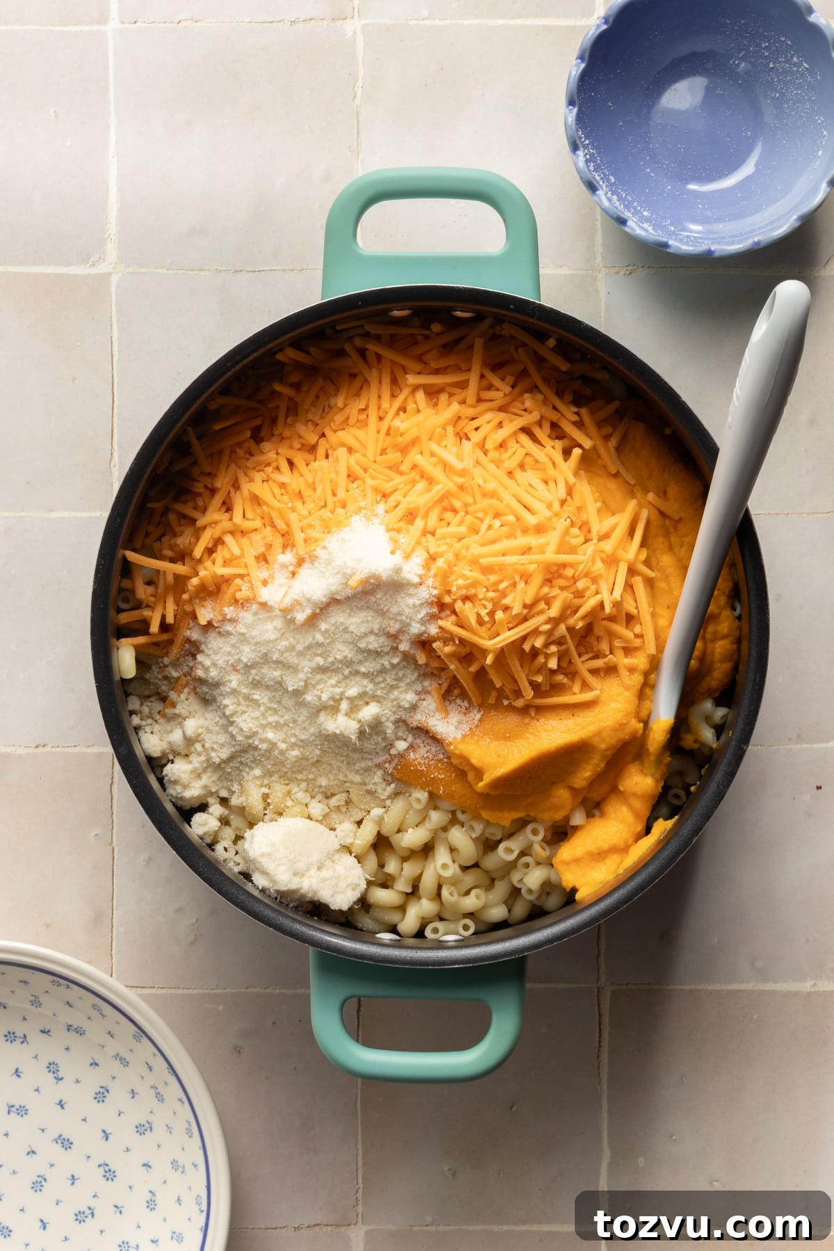 Creamy Hidden Vegetable Mac and Cheese Recipe 9 Blended veggies, cheese, and parmesan cheese being added to cooked pasta.