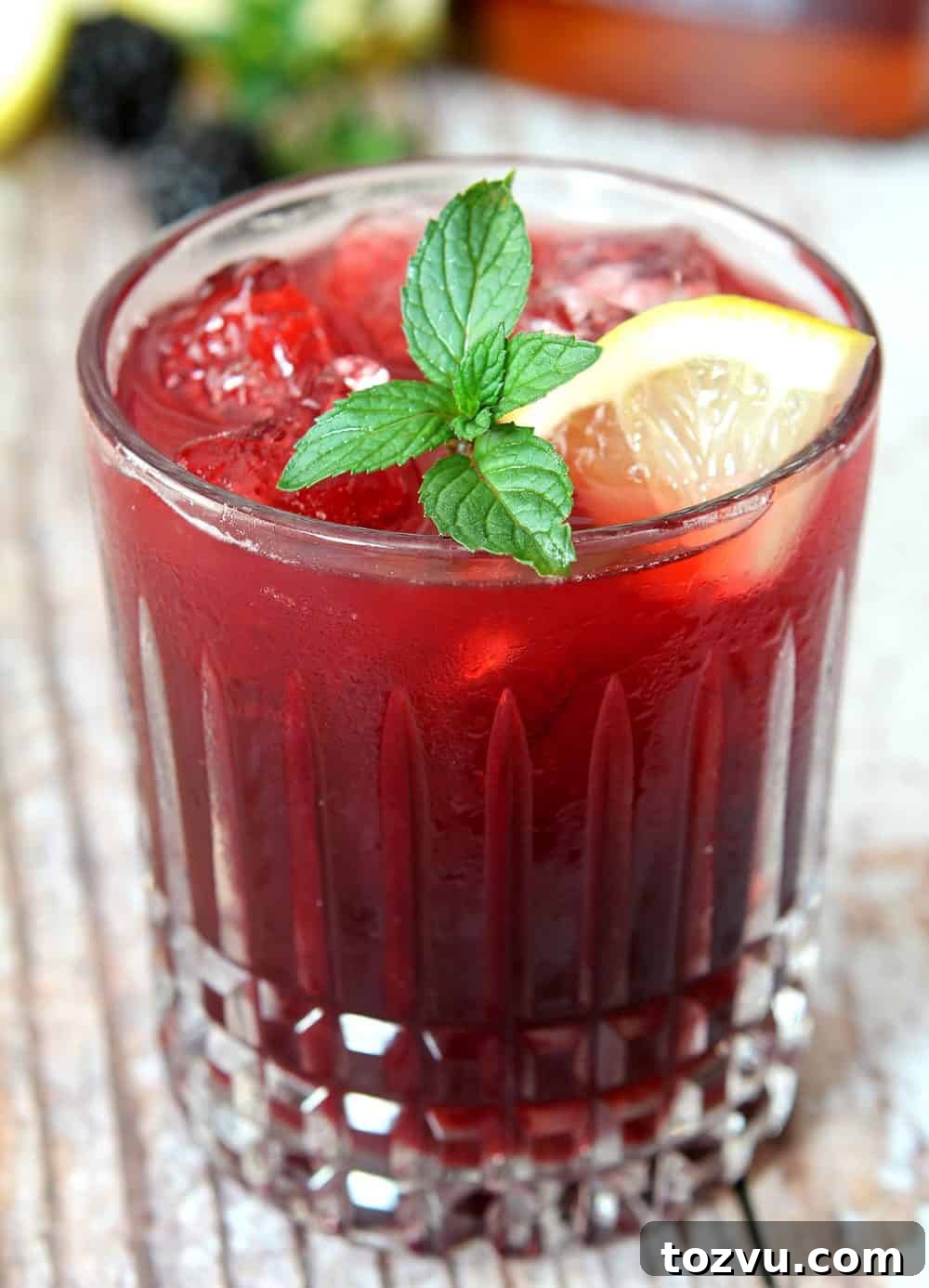 Closeup of Blackberry Smash Cocktail made with blackberries and whiskey, garnished with mint and lemon slice.