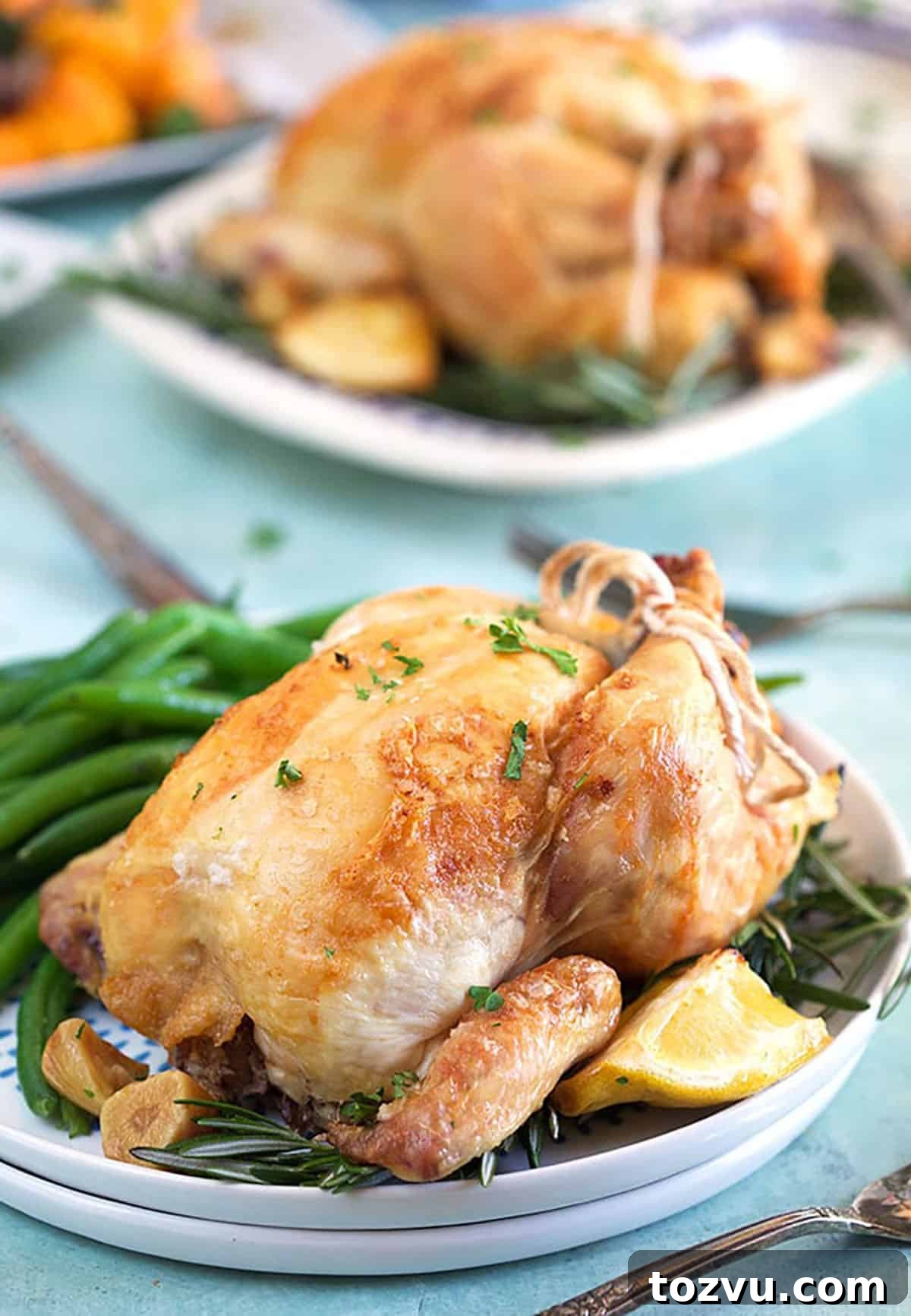 Herb-Roasted Cornish Game Hen with Crispy Skin 2 Cornish hen on a white plate with roasted lemon and green beans.