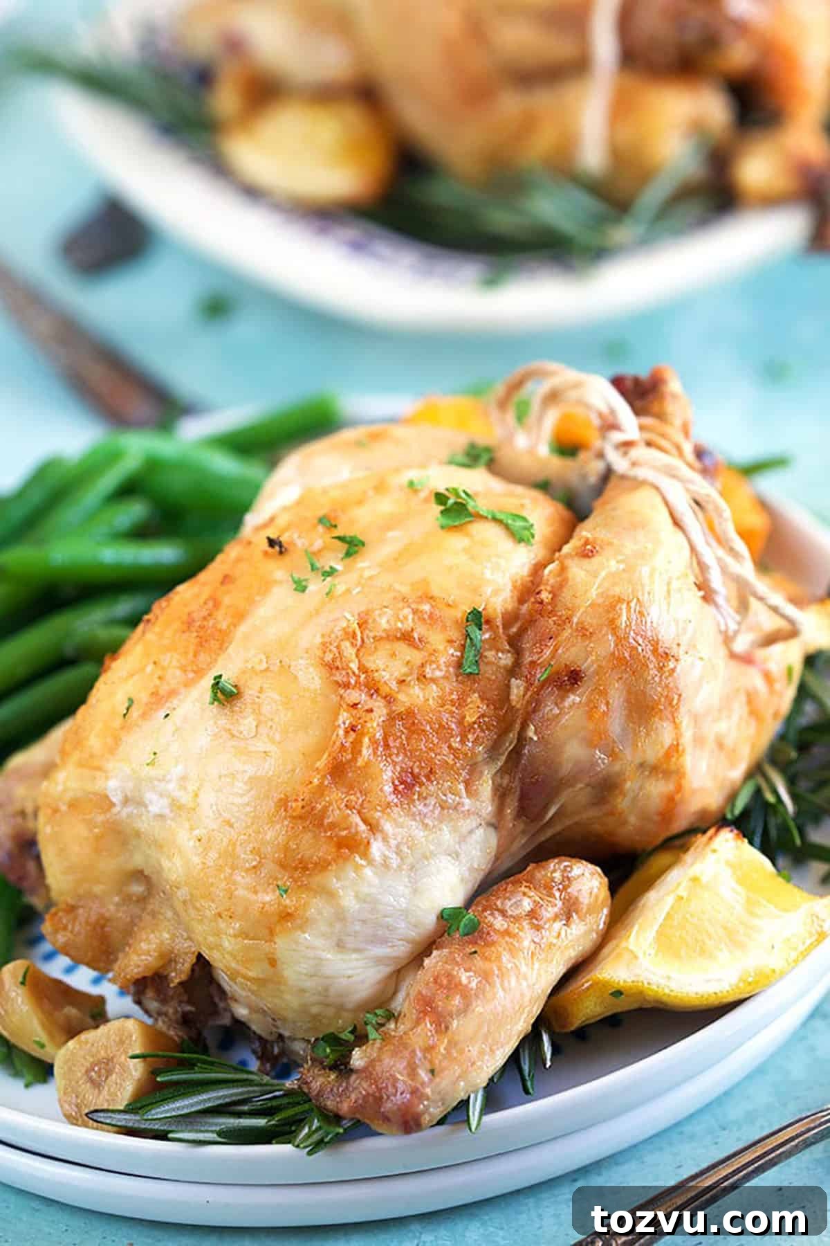 Herb-Roasted Cornish Game Hen with Crispy Skin 4 Close up of cornish hen on a white plate with a lemon wedge and green beans.