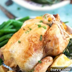 Herb-Roasted Cornish Game Hen with Crispy Skin 6 Close up of cornish hen on a white plate with a lemon wedge and green beans.