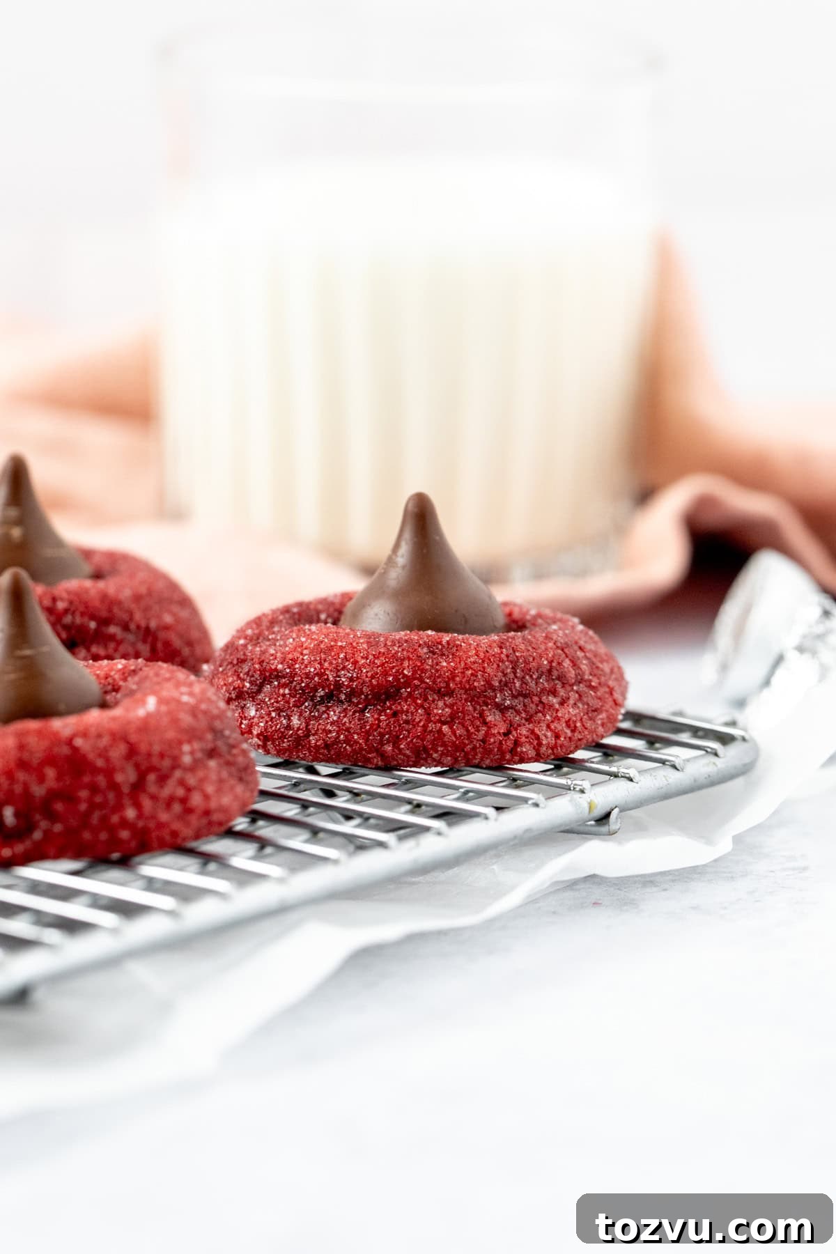 Red velvet Hershey's Kiss cookies on a cooling rack with a glass of milk