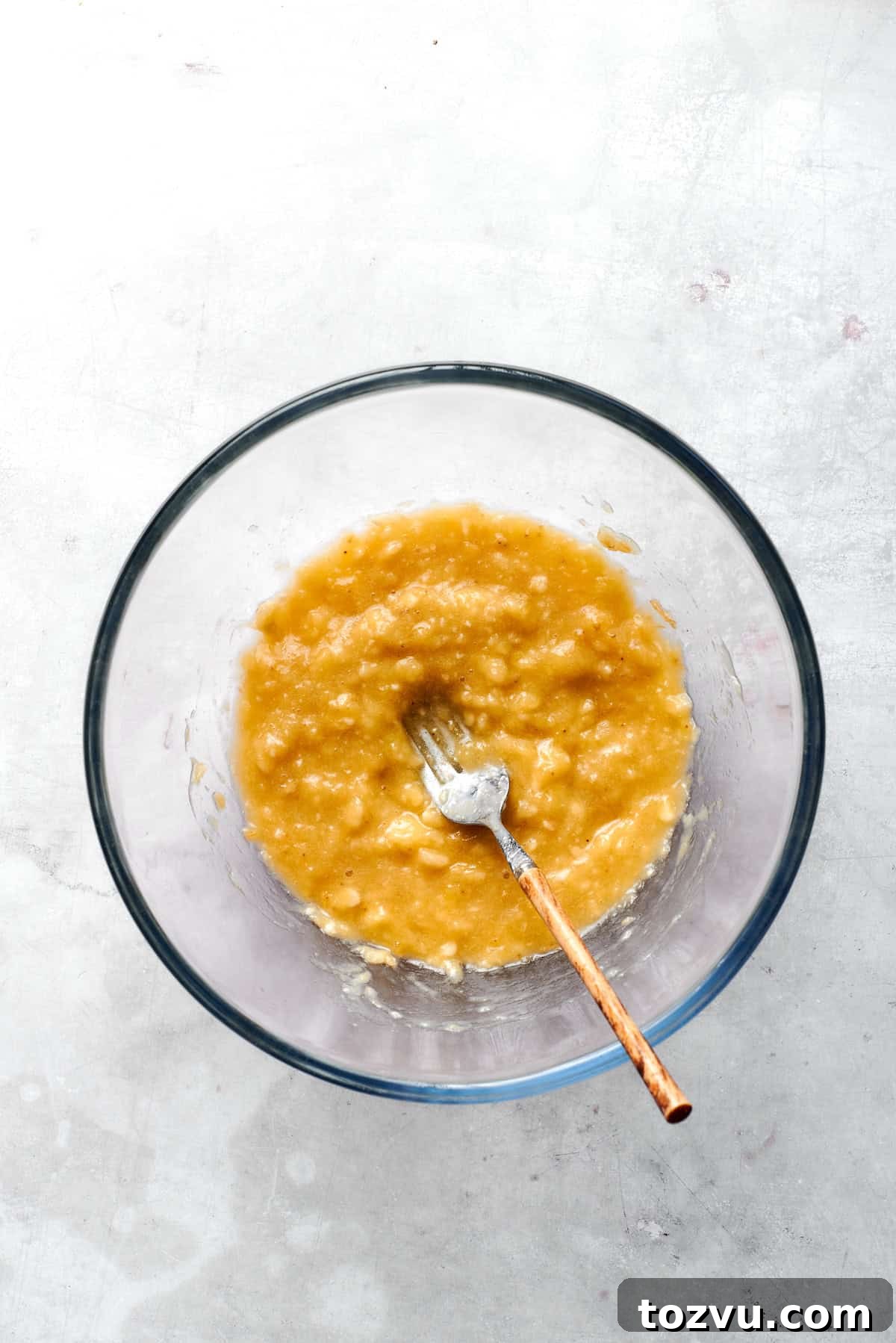 Bananas are mashed with a fork in a bowl.