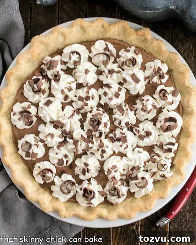 Overhead view of a French Silk Pie in a red ceramic pie plate with whipped cream and chocolate garnishes.