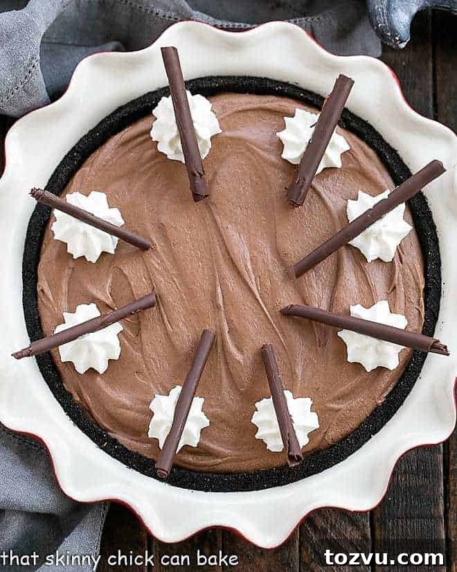 Frangelico French Silk Pie - a decadent chocolate pie topped with whipped cream and chocolate curls Frangelico French Silk Pie in a red ceramic pie plate with whipped cream and chocolate curl garnishes.