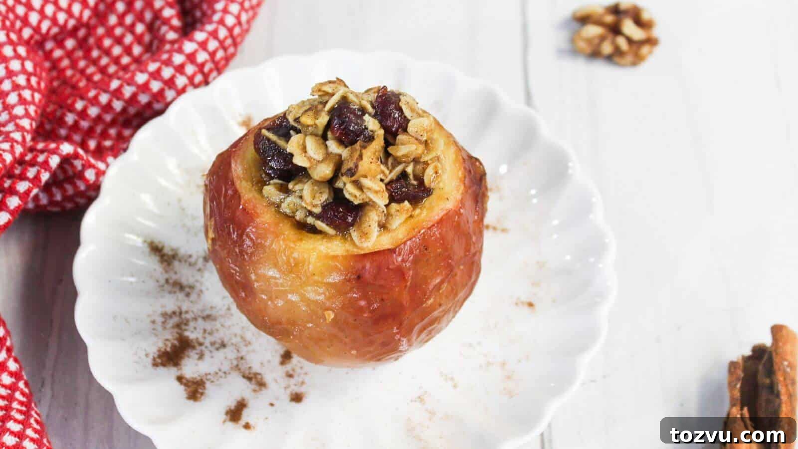 Air Fryer Baked Apples with Cinnamon and Brown Sugar 2 Baked apple in air fryer filled with oats and dried fruit on a white plate, next to a red-checkered cloth and cinnamon sticks.
