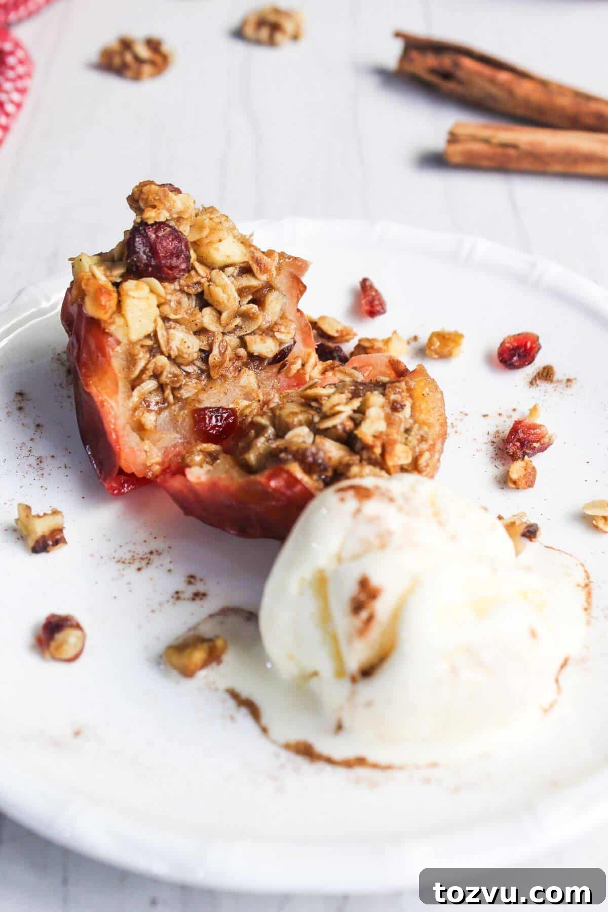 Air Fryer Baked Apples with Cinnamon and Brown Sugar 11 A warm, air-fried baked apple half topped with a crunchy oat and nut crumble, elegantly paired with a scoop of creamy vanilla ice cream on a white plate.
