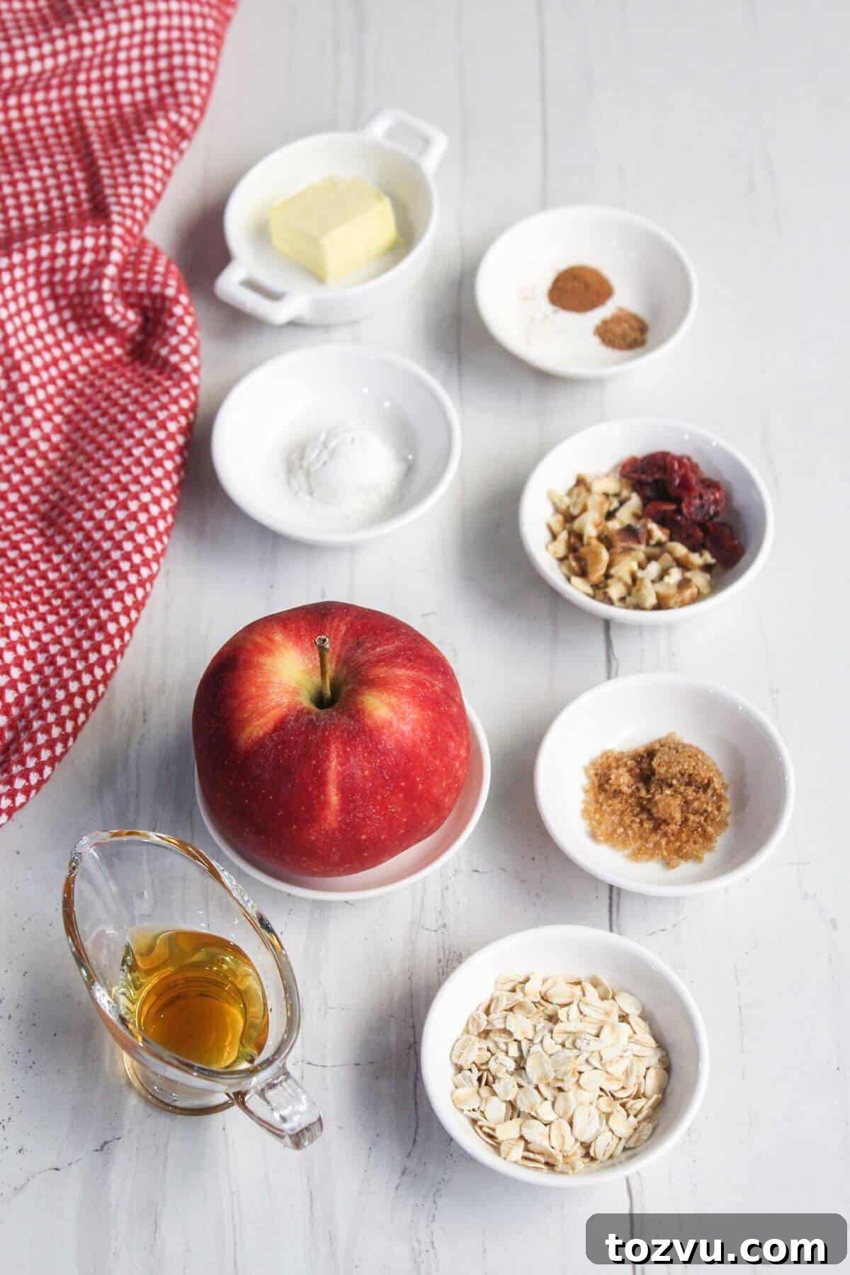 Air Fryer Baked Apples with Cinnamon and Brown Sugar 3 Ingredients on a table: apple, oats, butter, brown sugar, nuts, cranberries, spices, baking powder, and syrup. A red checkered cloth sits to the side. Perfect for making a baked apple in the air fryer!