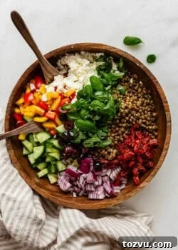 Mediterranean lentil salad in a wood bowl with wood spoons and a napkin on the side.