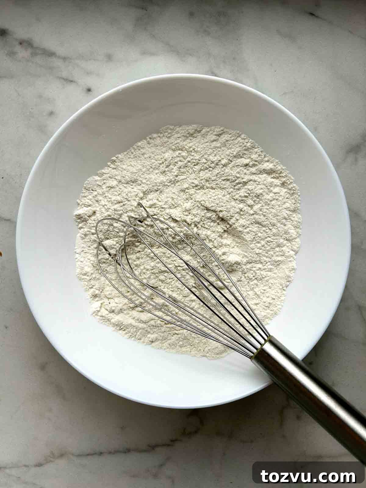 Fluffy Dairy-Free Pancakes Without Milk 4 flour mixture whisked in white bowl.