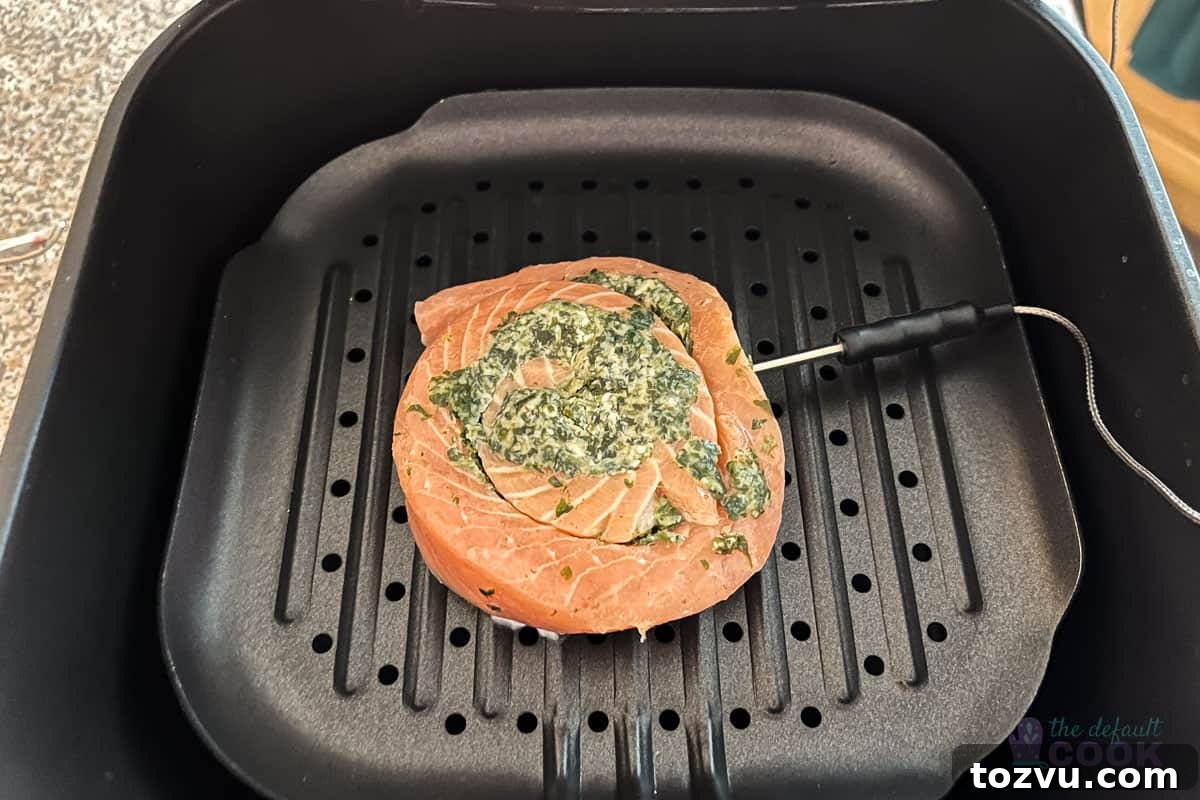 Trader Joe's Salmon Pinwheels Recipe with Feta and Spinach 4 A raw salmon pinwheel stuffed with spinach and cheese placed in an air fryer grill pan, with a temperature probe inserted into the side.