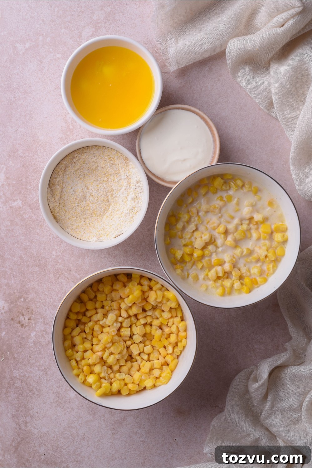 An assortment of ingredients including bowls of melted butter, creamed corn, whole corn kernels, and muffin mix.