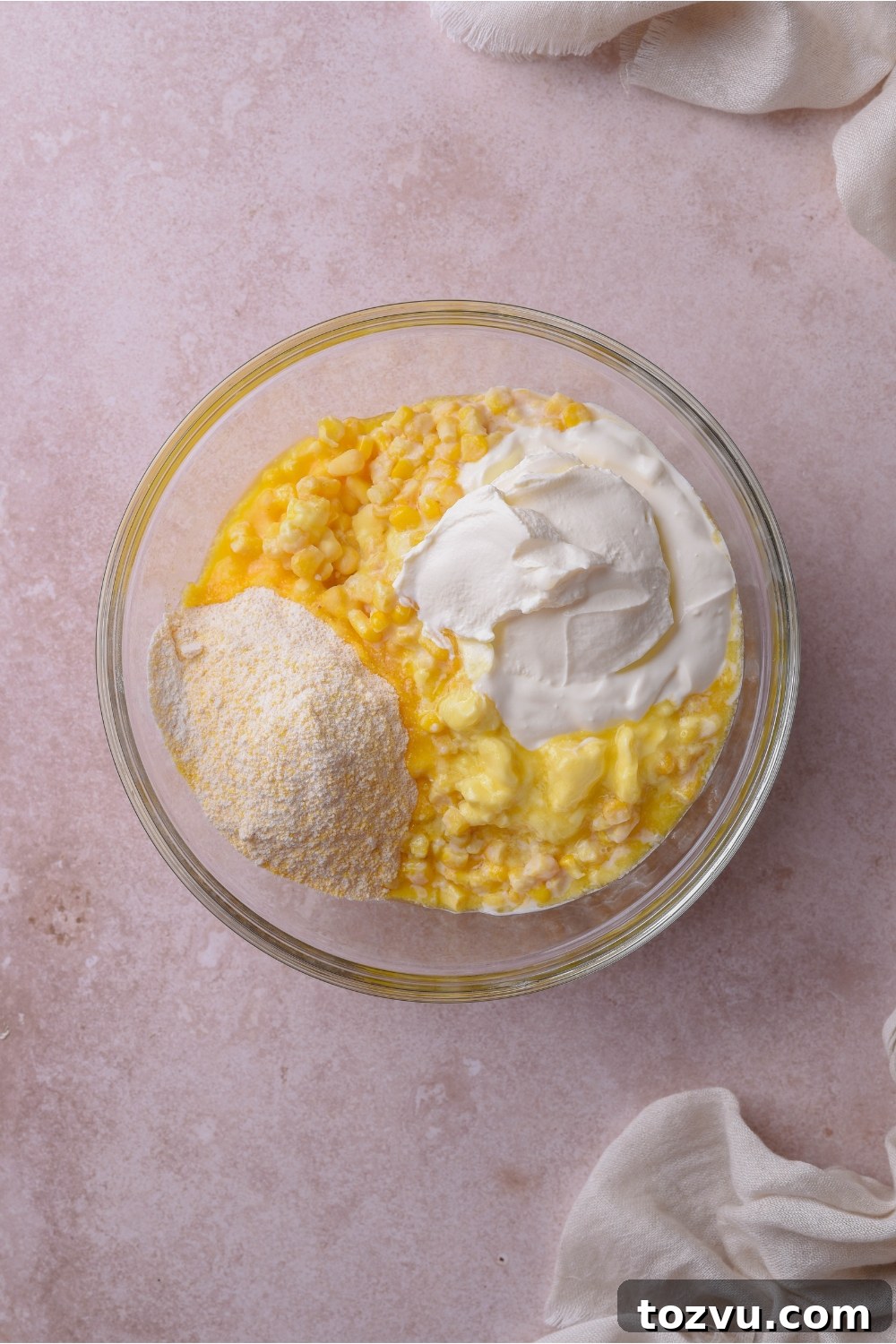 A clear bowl filled with creamed corn, sour cream, and dry muffin mix.