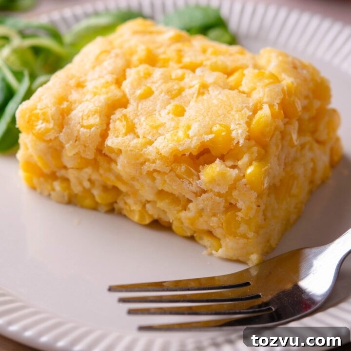 A slice of Jiffy corn casserole on a white plate with a fork on it.