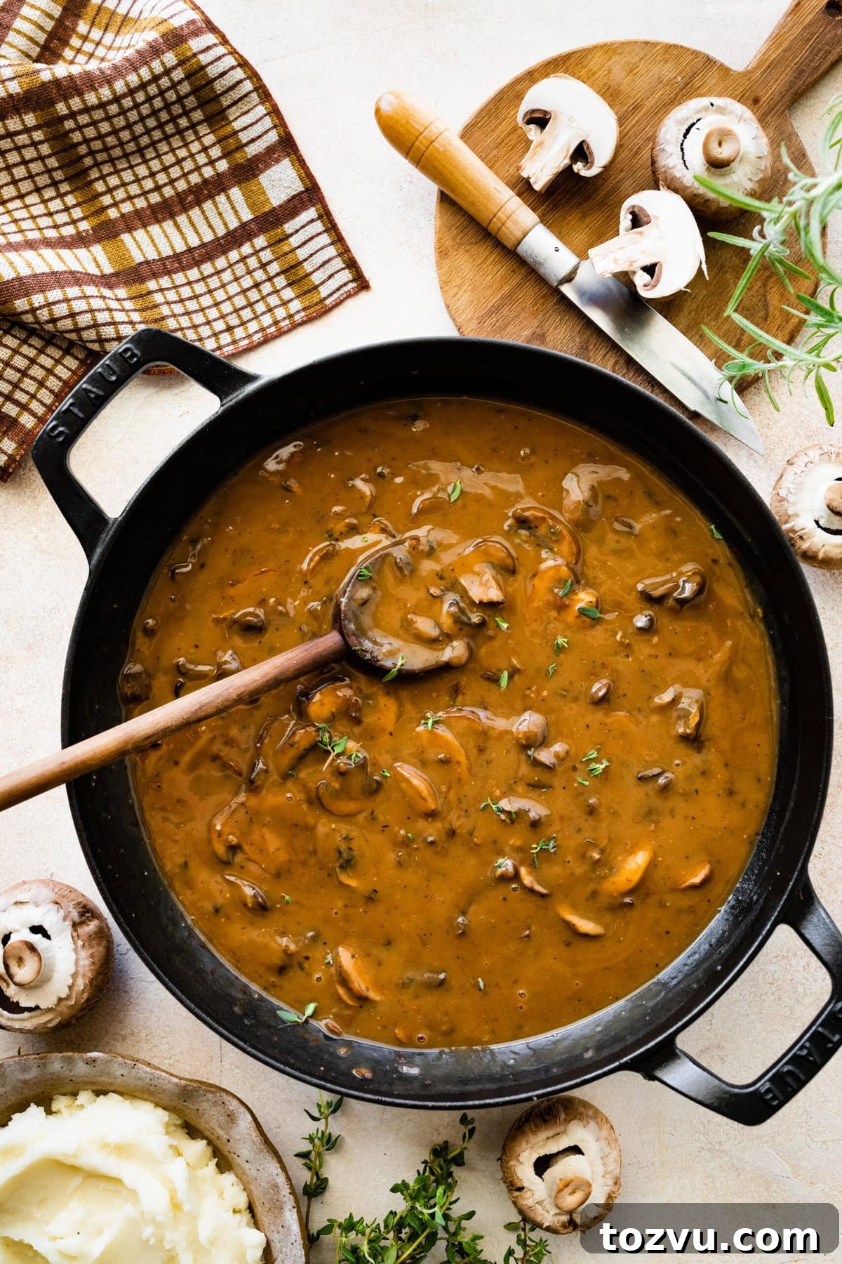 How to Make Mushroom Gravy from Scratch 13 Easy mushroom gravy in a skillet pan with wooden spoon. Mushrooms on the side.