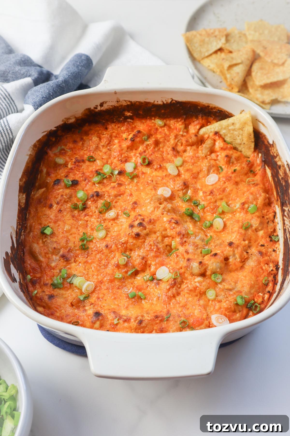 white baking dish with chip in the buffalo dip topped with green onion