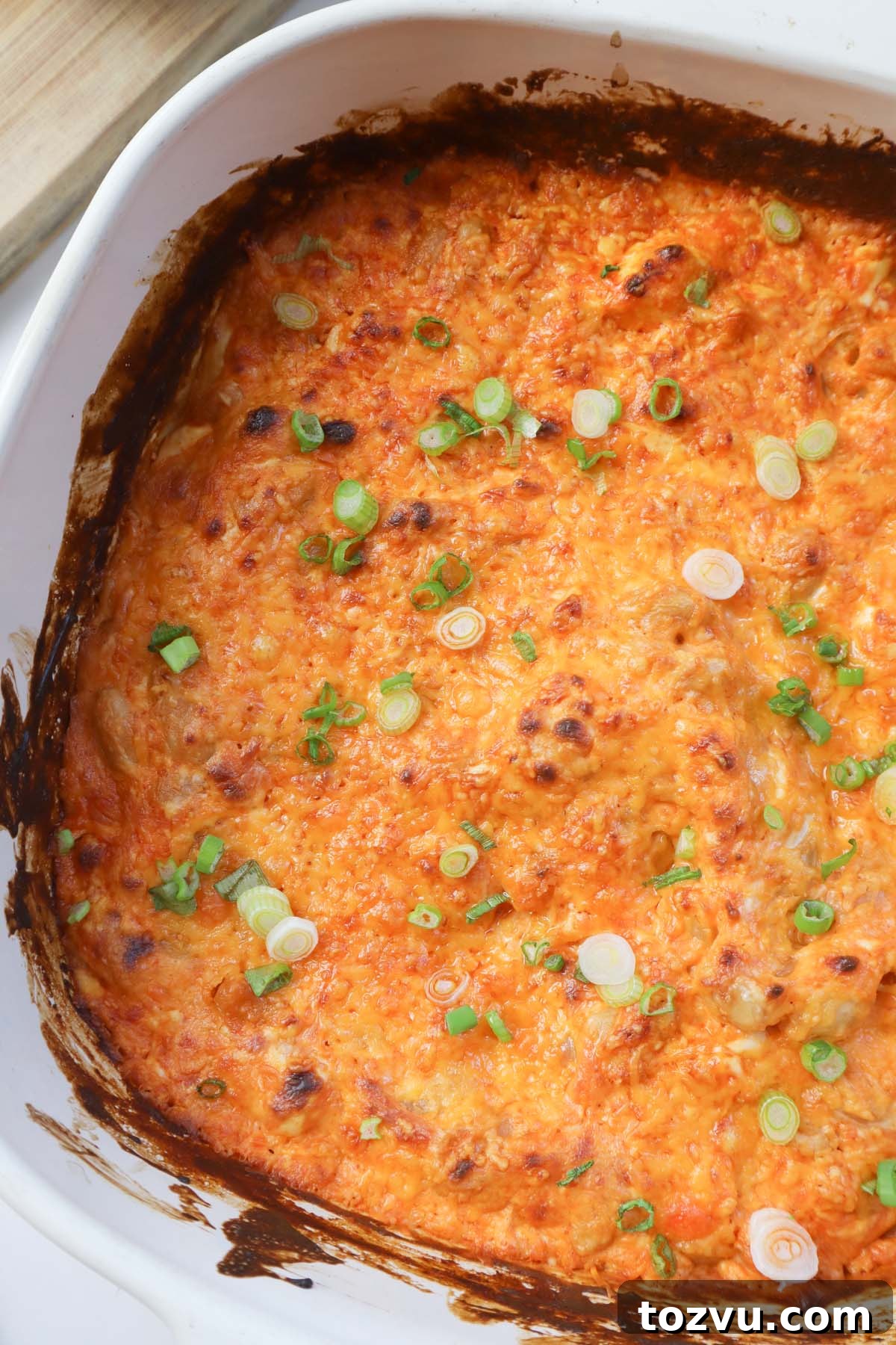 white glass baking dish with buffalo dip topped with green onion