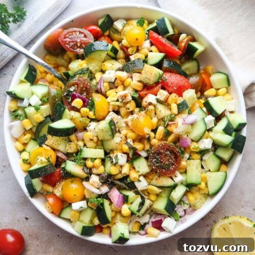 bowl with tomato corn cucumber salad tossed in lemon juice and olive oil.