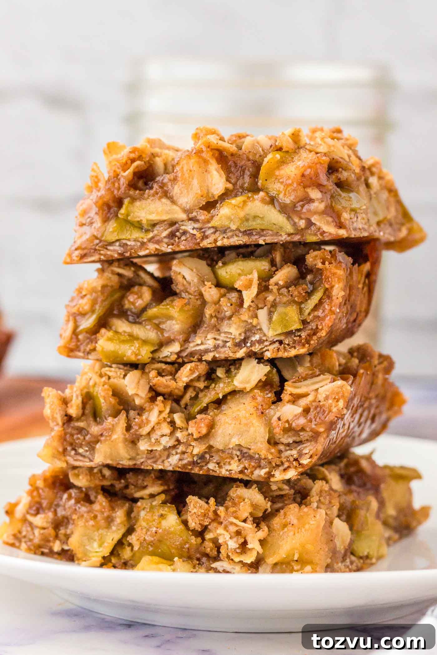 Stack of 4 apple crumble bars on a plate. The bars have an oatmeal crust and crumble topping with a layer of apple pie filling in between.