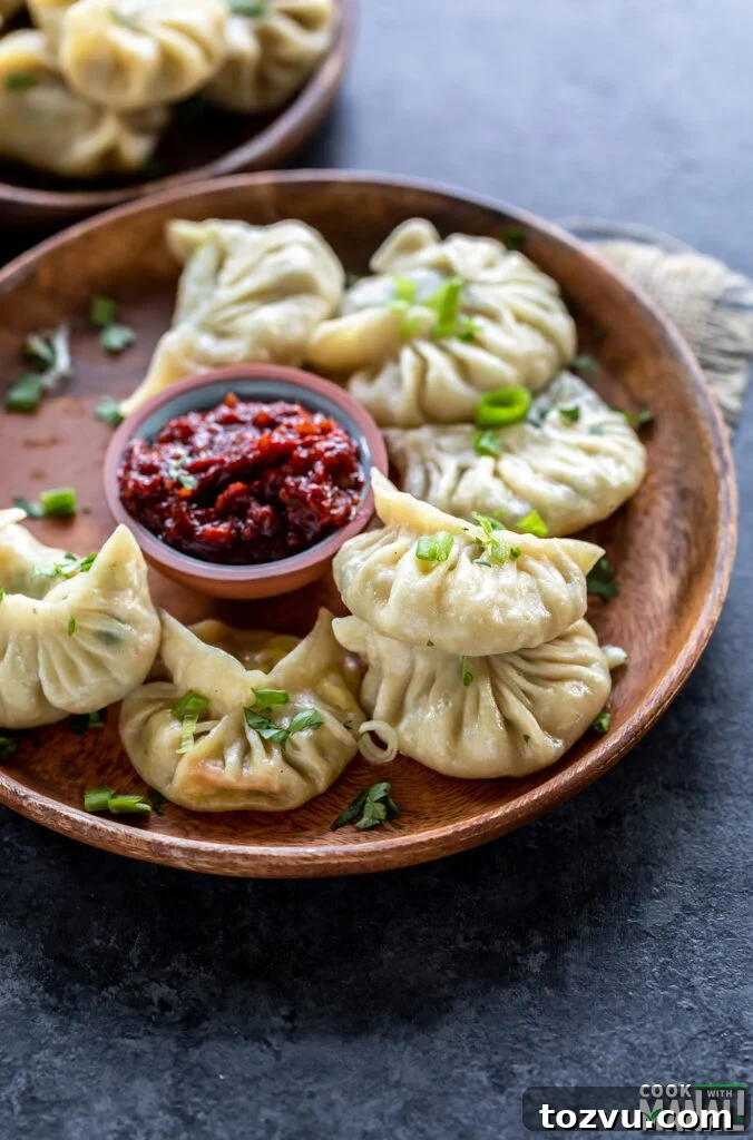 steamed momos placed on a wooden plate with a bowl of hot sauce on the side