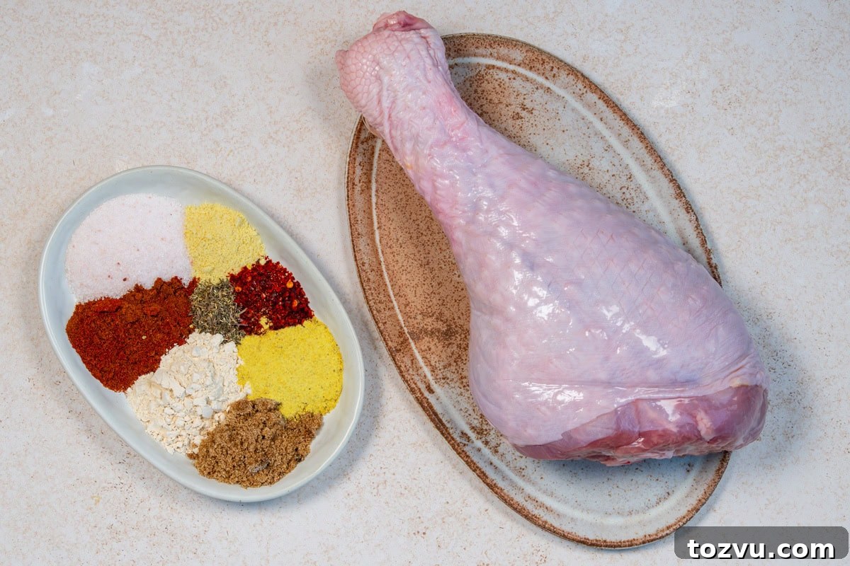 Slow-Cooker Turkey Legs with Savory Herb Glaze 5 A raw turkey leg on an oval plate sits beside a dish containing piles of various spices and seasonings, including yellow, red, white, and brown powders, on a light-colored surface.