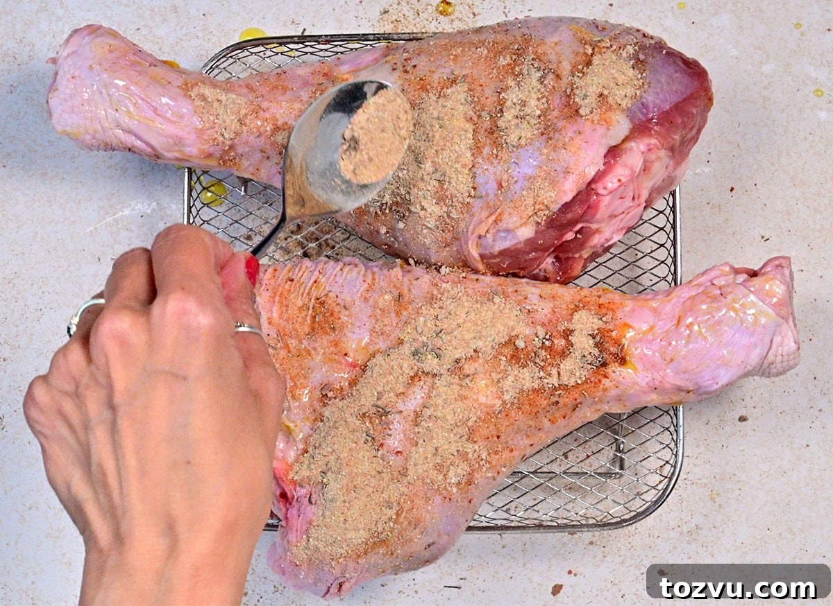 Slow-Cooker Turkey Legs with Savory Herb Glaze 6 A hand sprinkles seasoning onto two large, raw turkey legs placed on a wire rack, preparing them for cooking.
