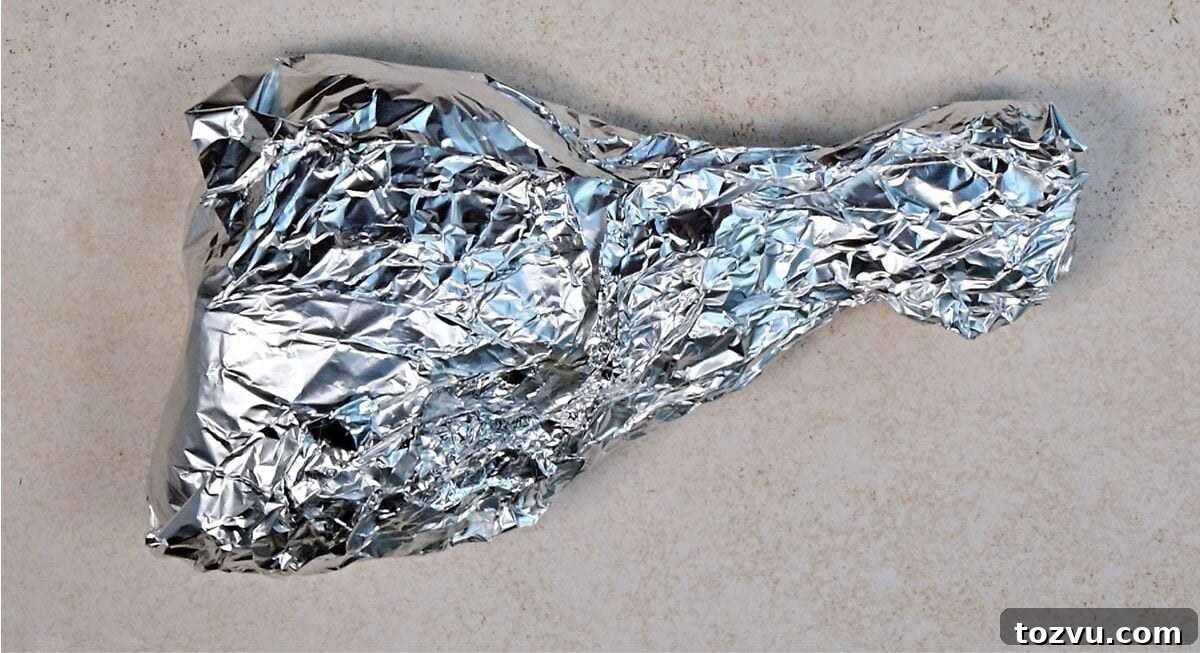 Slow-Cooker Turkey Legs with Savory Herb Glaze 7 A crumpled sheet of aluminum foil is shaped like a drumstick and placed on a light, textured surface.