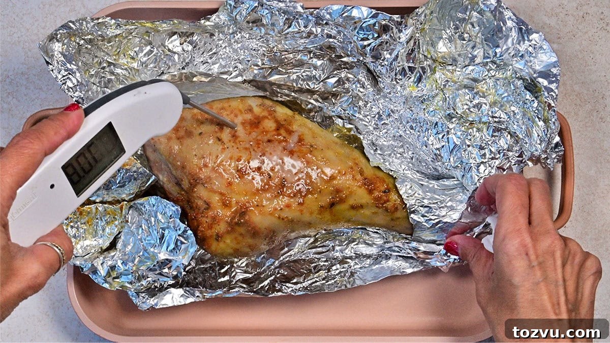 Slow-Cooker Turkey Legs with Savory Herb Glaze 8 A person checks the temperature of cooked chicken breast wrapped in aluminum foil using a digital meat thermometer. The chicken rests in a pink baking tray on a light countertop.