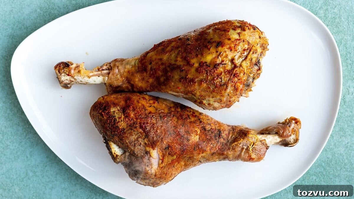 Slow-Cooker Turkey Legs with Savory Herb Glaze 10 Two seasoned and roasted turkey legs placed side by side on a white oval plate, set against a light green background.