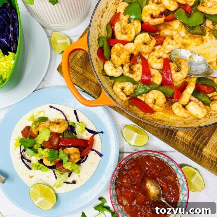 Mexican prawn fajitas being served from a skillet pan. Fajita is loaded with lettuce, shredded red cabbage, prawns, guacamole and tomato salsa.