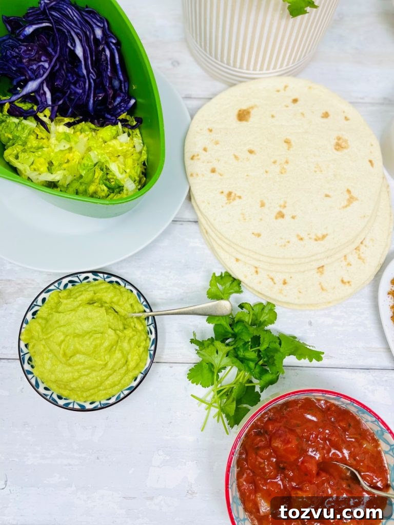 20-Minute Shrimp Fajitas with Peppers and Lime 4 ingredients to serve with king prawn fajitas - pile of soft flour tortilla wraps, bowl of guacamole, bowl of roast tomato salsa, shredded lettuce and red cabbage