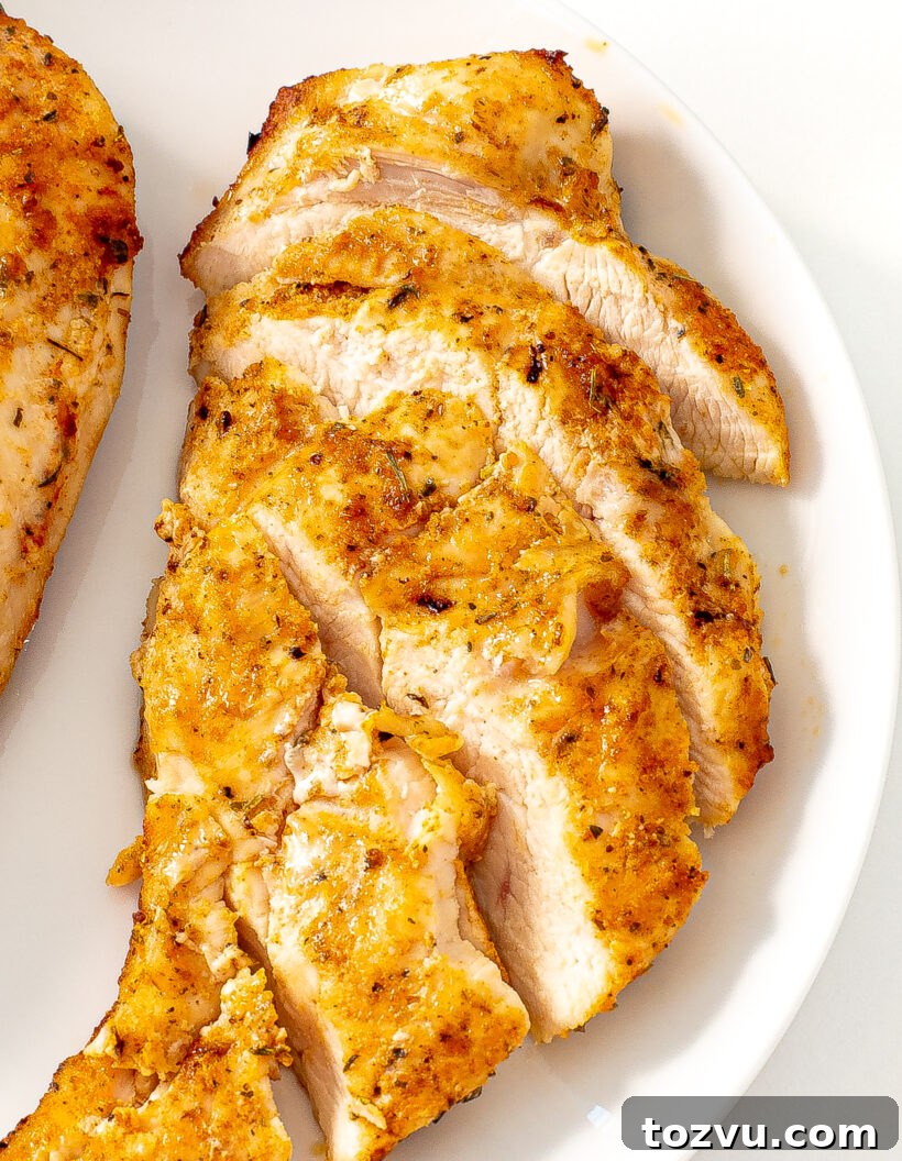 Juicy Air Fryer Chicken Breast Recipe 6 Sliced chicken breast on a white plate with more chicken next to it.