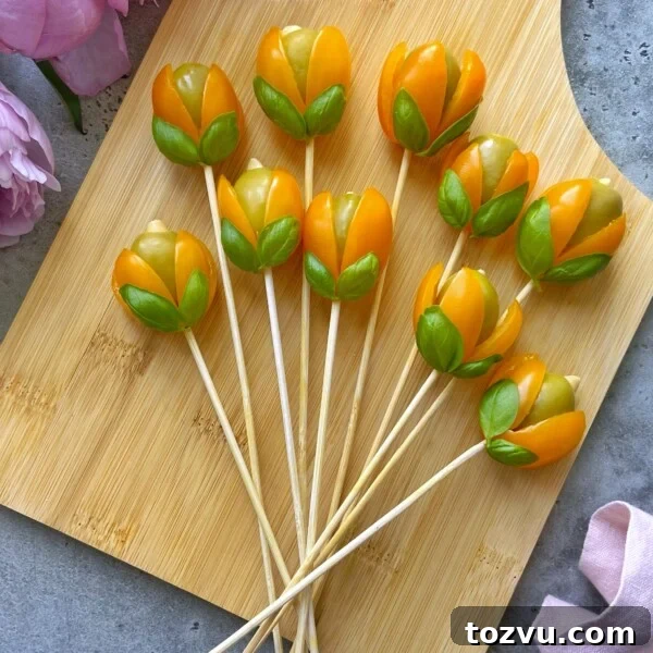 Olive appetizer sticks with cherry tomatoes and green leaves arranged to look like tulips on a wooden board.