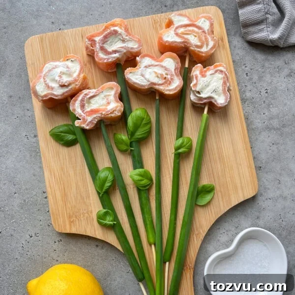 Sushi-style smoked salmon roulade bites arranged with cream cheese centers and garnishes on a wooden board.