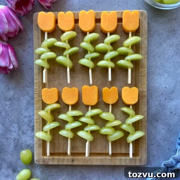 Cheese and grape skewers arranged to resemble flowers on a wooden board.