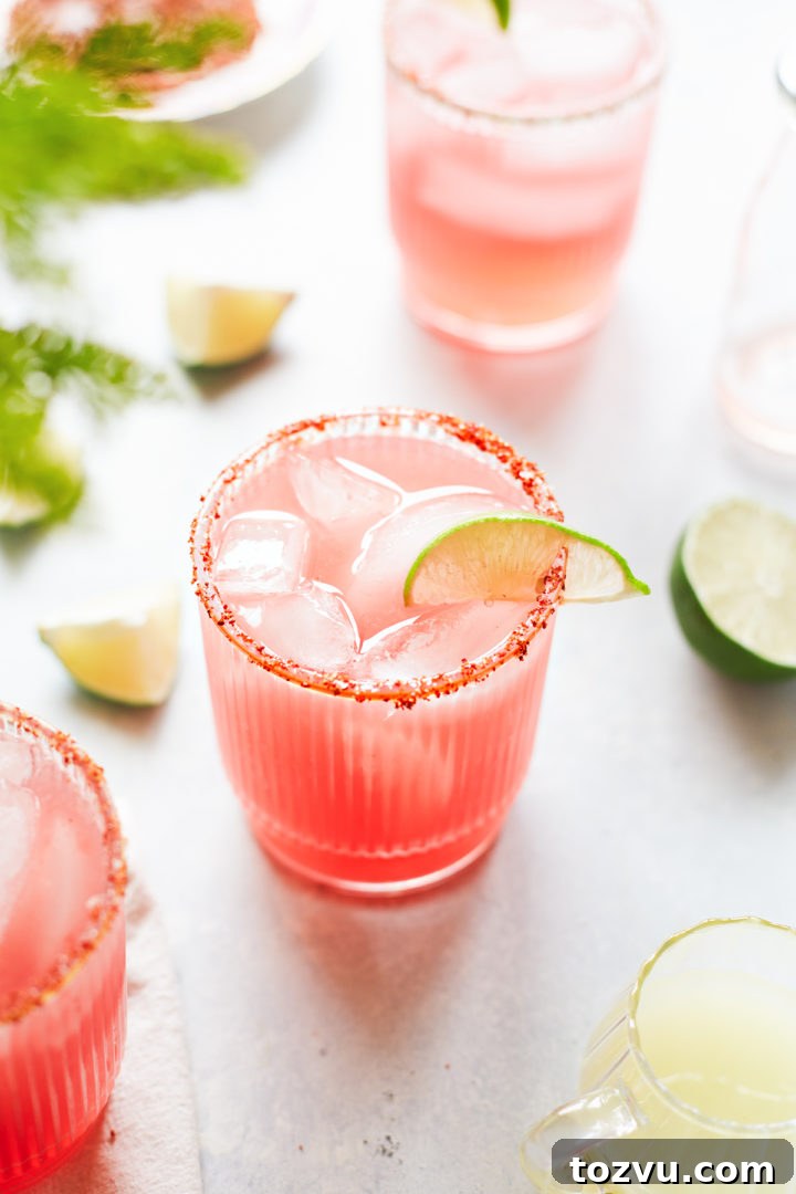 three glasses of watermelon margarita with a spicy salt rim and lime garnishes
