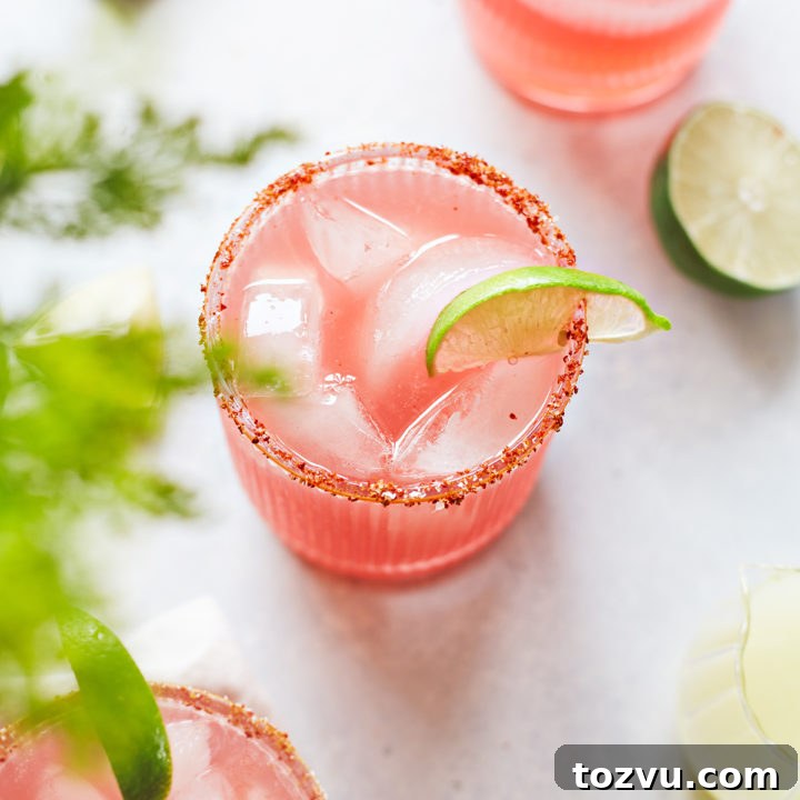 three glasses of watermelon margarita with a spicy salt rim and lime garnishes