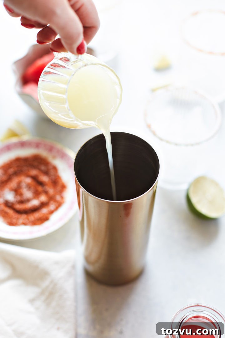 woman adding lime juice to a cocktail shaker with ingredients for a watermelon margarita