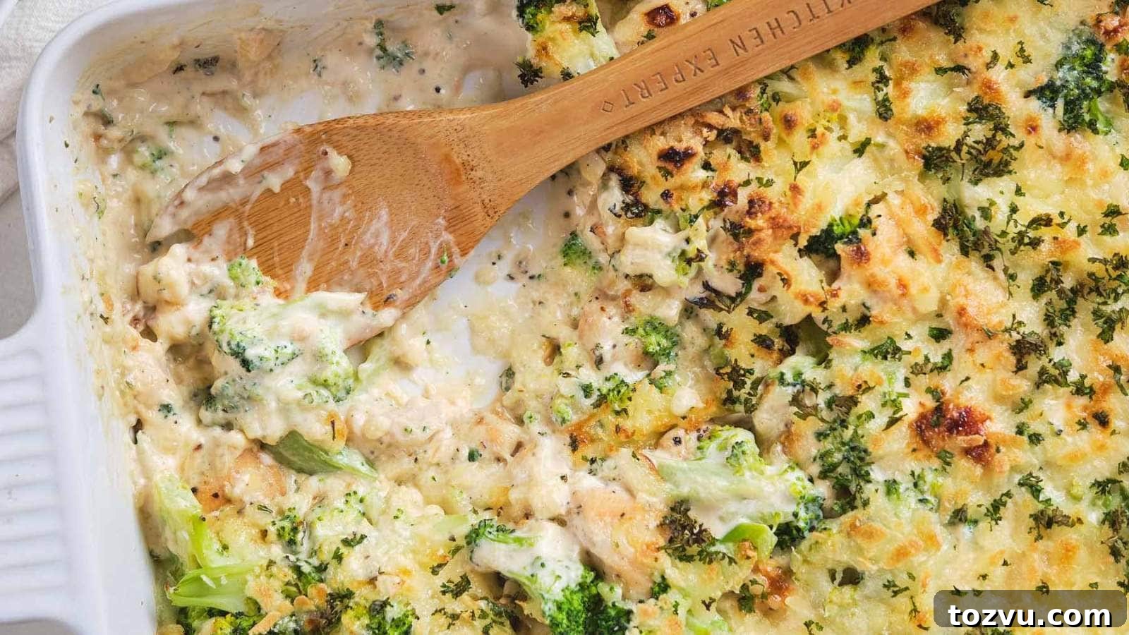 17 Thanksgiving Recipes Ready in Minutes 15 A wooden spoon scooping chicken broccoli alfredo casserole out of a serving dish.